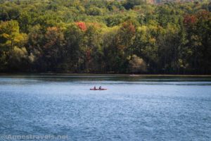 A canoe paddles on Canadice Lake below fall colors, New York